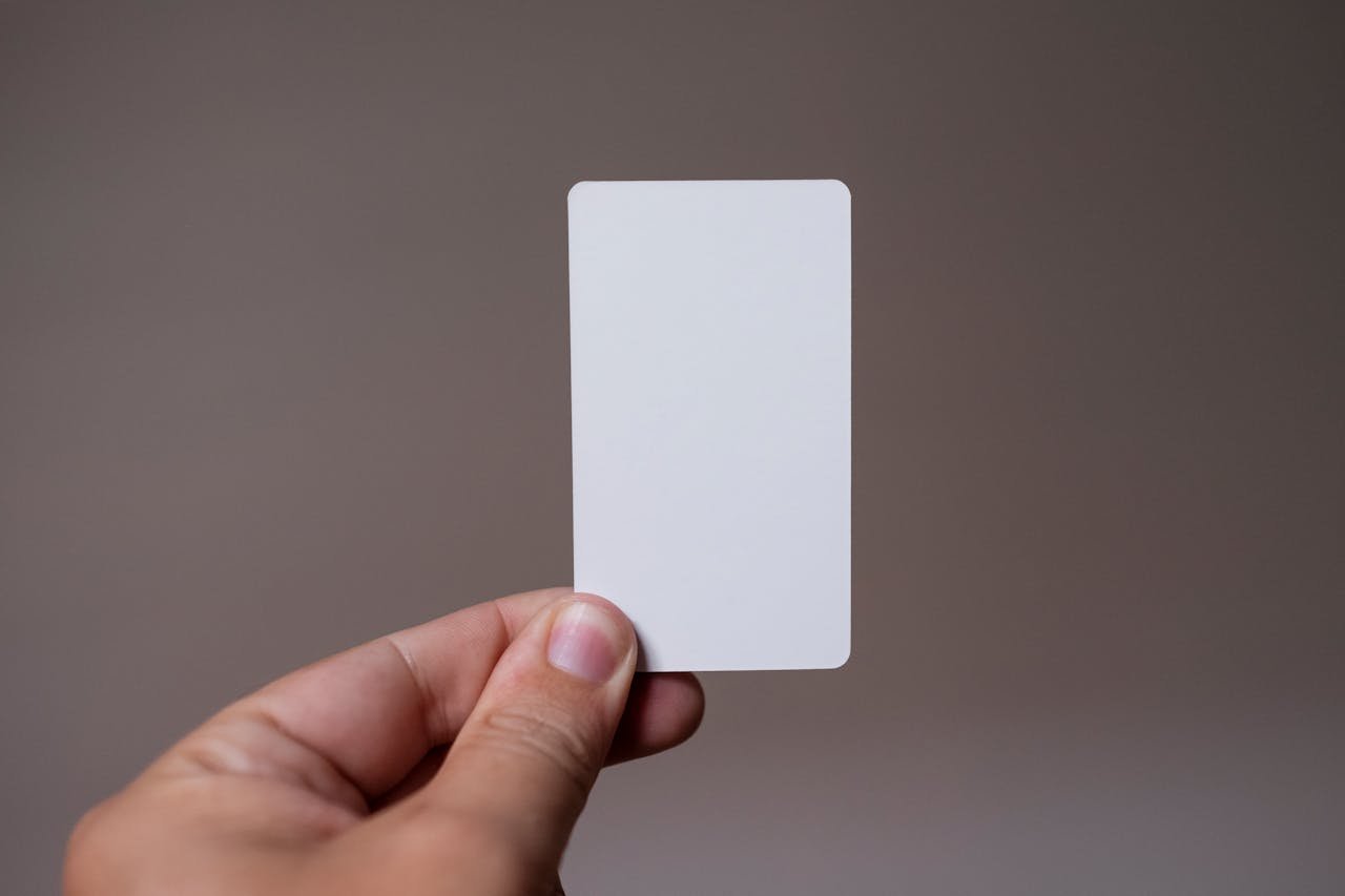 Close-up of a hand holding a blank white card with a neutral background, perfect for mockups.