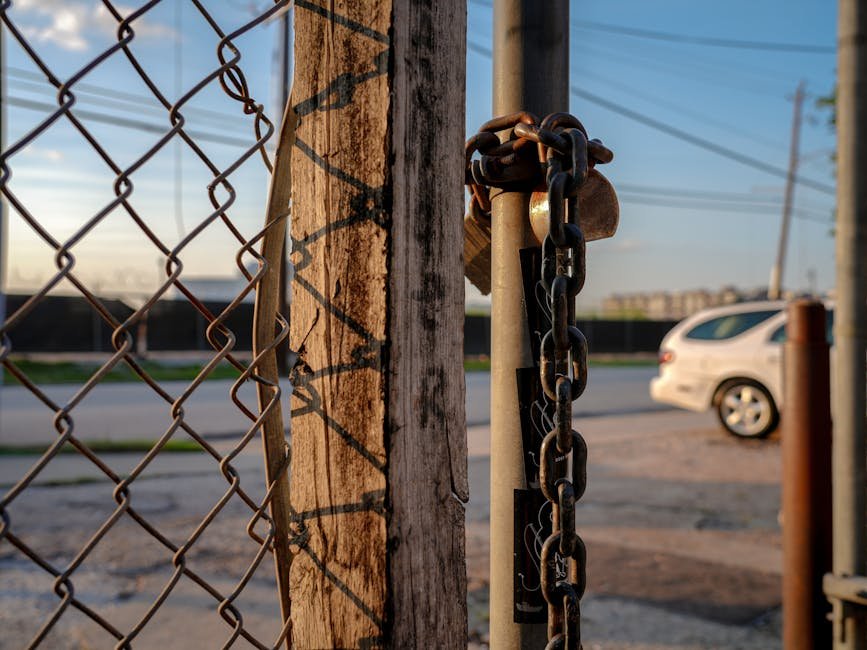 Close-up of a chain and padlock on a fence post with a car in the background in Houston.